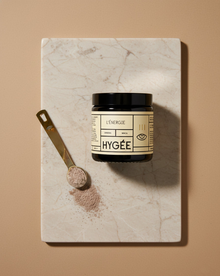 Top‑down still life of a HYGÉE L’Énergie jar on a pale marble board with a brass scoop of fine taupe powder and a soft spill under crisp studio light.
