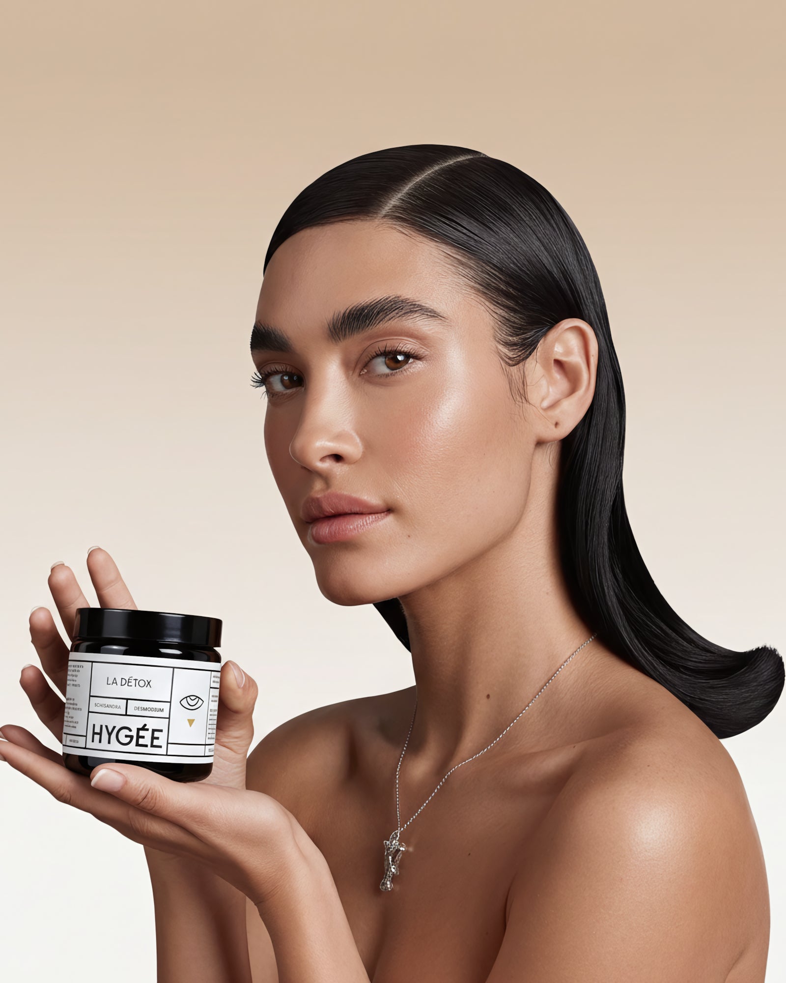 A woman with sleek dark hair and luminous skin delicately holds a HYGÉE La Détox jar near her shoulder against a gradient beige backdrop. A refined studio portrait with gentle highlights and minimal styling.