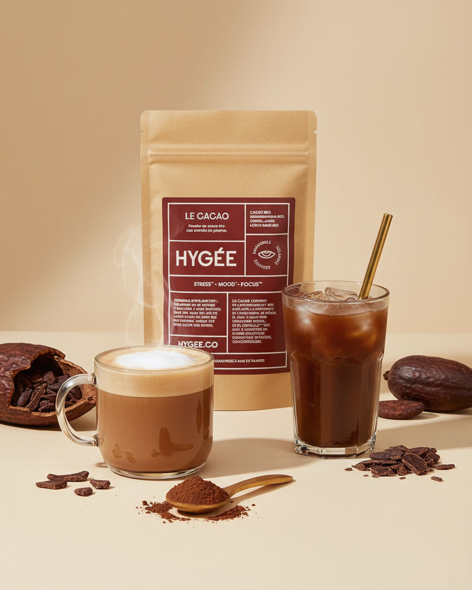 Allnord’s HYGÉE Le Cacao pouch sits behind a steaming hot cacao and an iced cacao with a gold straw, surrounded by spoons of powder and broken chocolate. A bright countertop scene with creamy foam and cool glass reflections.​