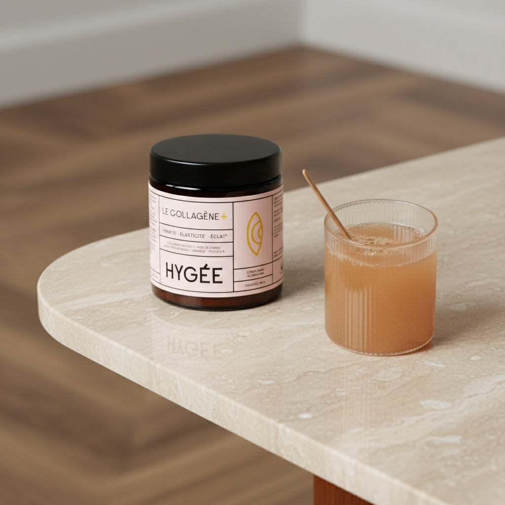 Allnord’s HYGÉE Le Collagène+ jar sits beside a ribbed glass of mixed collagen drink with a gold spoon on a creamy stone table. A calm kitchen‑counter scene with gentle reflections and natural wood in the background.​